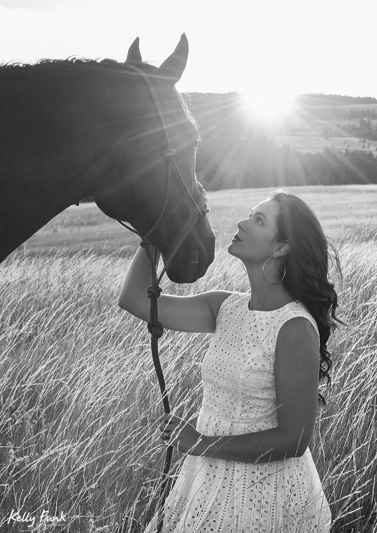 A beautiful woman and her horse pose in a field at sunset for a portrait during sunset on the ranch near Kamloops, British Columbia, Canada