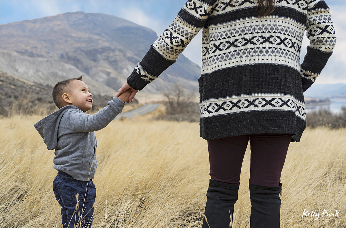 A mother leads her son through the tall grass during a family shoot, near Kamloops, British Columbia, Canada