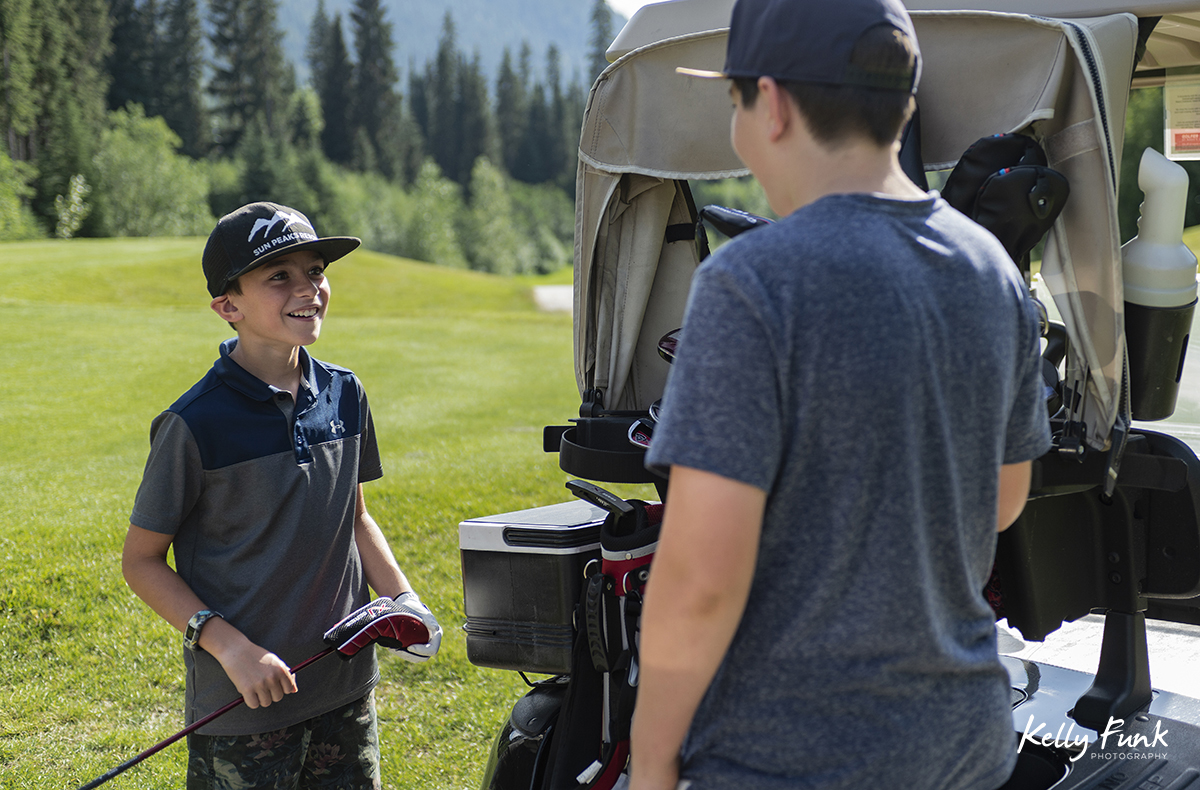 Two boys laugh while golfing at the Sun Peaks Resort golf course, north east of Kamloops, British Columbia, Thompson Okanagan region, Canada