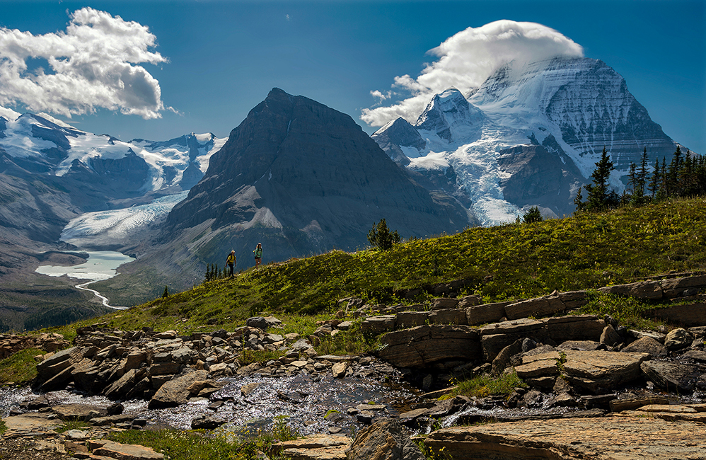 Two hikers traverse a ridge with Mount Robson towering in the background captured by Kelly Funk Photography on a gorgeous summer day in the Thompson Okanagan region of British Columbia Canada